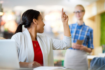 Young businesswoman turning back while looking at waitress and snapping her fingers