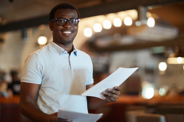 Obraz premium Young successful businessman with papers looking at you in modern cafe during work