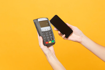 Close up cropped photo female holding in hands wireless modern bank payment terminal to process and acquire credit card payments mobile phone isolated on yellow background. Copy space for advertising.
