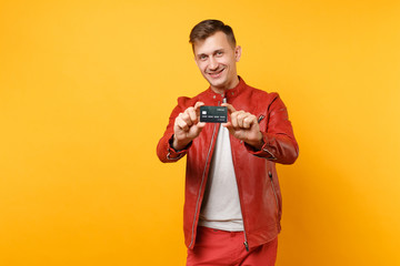 Portrait vogue smiling handsome young man in red leather jacket t-shirt hold bank credit card isolated on bright trending yellow background. People sincere emotions lifestyle concept. Advertising area