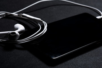 white headphones on a black mobile phone lying on a background of black leather