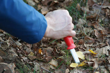 A mans hand with knife stick in ground.