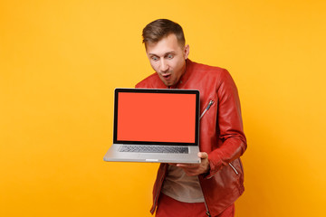Portrait vogue fun young man in red leather jacket, t-shirt hold laptop pc computer blank empty screen isolated on bright yellow background. People sincere emotions lifestyle concept. Advertising area