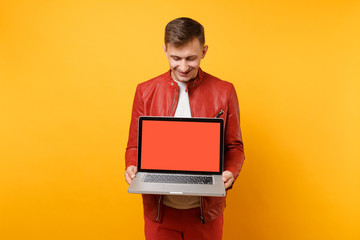 Portrait vogue fun young man in red leather jacket, t-shirt hold laptop pc computer blank empty screen isolated on bright yellow background. People sincere emotions lifestyle concept. Advertising area