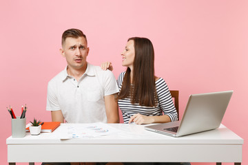 Two young business woman man colleagues sit at white desk isolated on pastel pink background....