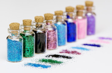 Small bottles with multicolored sparkles and scattered spangles on white background