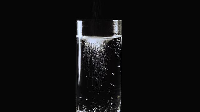 Aspirin Tablet Falls to the Bottom of the Glass With Water, Air Bubbles Rise From the Bottom of the Glass in a Glass of Mineral Water and Carbon Dioxide is Rising on a Black Background Slow Motion