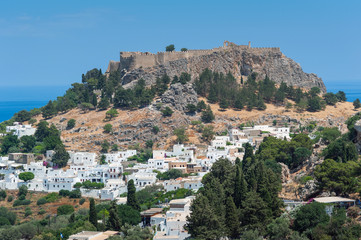 Fototapeta na wymiar Distant view at Lindos Town and Castle with ancient ruins of the Acropolis on sunny warm day. Island of Rhodes, Greece.