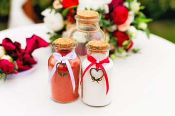 A close-up of three transparent jars, two of which are filled with sand of various colors and decorated with ribbons with hearts