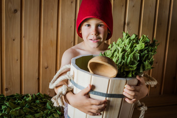 Portrait of a little boy of 5 years wrapped in a towel at preschool age, sitting in a sauna and...