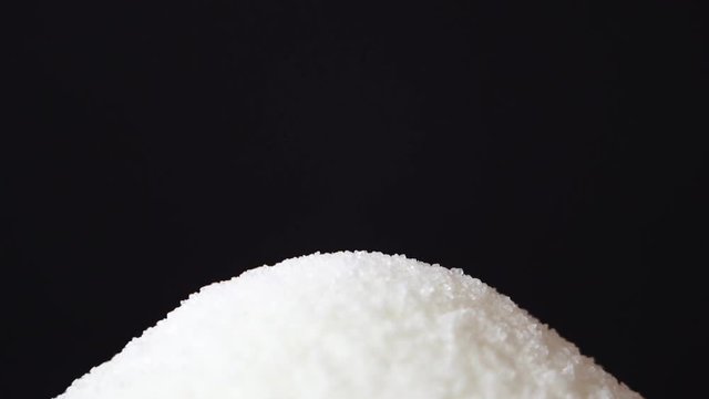 White cane sugar from teaspoon is fall down on a black background. Bottom view. Sugar falls straight into the camera on black background. Slow motion, high speed camera, 120fps