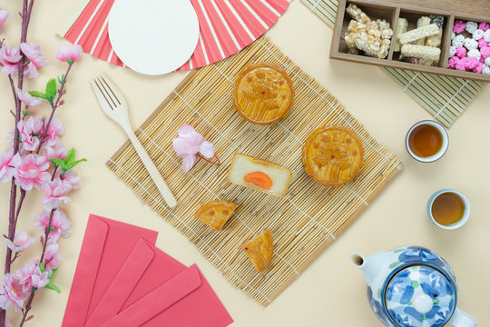 Table top view aerial image of decorations Chinese Moon Festival or lunar new year background concept.Flat lay essential meal set for coffee break of sweet cake & tea with blossom on yellow paper.