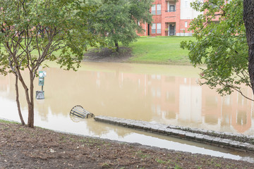 Flooded riverside pathway near riverside apartment complex in suburban Dallas Fort Worth, Texas, USA. Swamped dog waste station and outdoor steel garbage receptacle