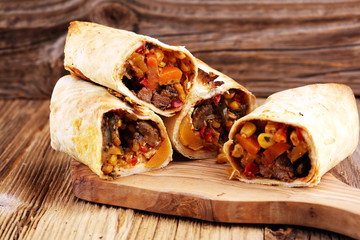 Burritos wraps with beef and vegetables on wooden background. Beef burrito, mexican food