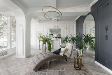 Morning in luxurious light interior in hotel. Bright and clean interior design of a luxury living room with parquet wood floors, fireplace, sofa and houseplant. Stucco on walls