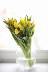 A bouquet of yellow tulips in a vase on the windowsill. A gift t