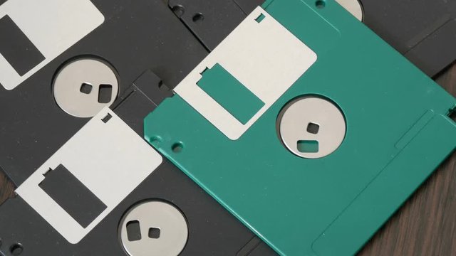 Close up top view of many 3.5 inch computer floppy disks or diskette scattered on flat surface vintage technology. A woman's hand picks up floppy disks