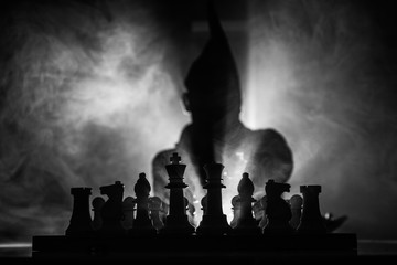 Fototapeta na wymiar Man playing chess. Scary blurred silhouette of a person at the chessboard with chess figures. Dark toned foggy background.