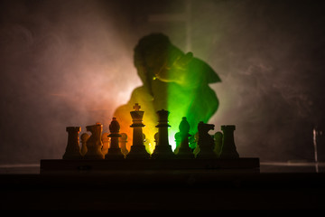 Man playing chess. Scary blurred silhouette of a person at the chessboard with chess figures. Dark toned foggy background.