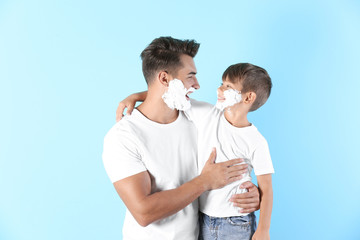 Naklejka premium Father and son with shaving foam on faces against color background