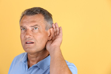 Fototapeta premium Mature man with hearing problem on color background. Space for text