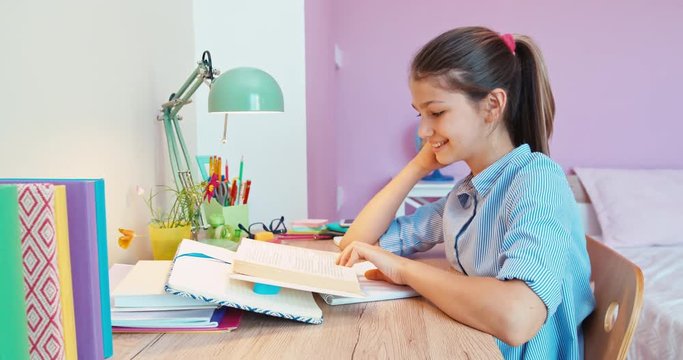 Cheerful school girl reading book at the table. Dolly shot
