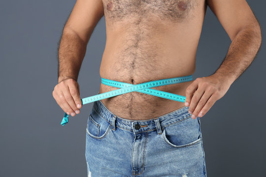 Overweight man with measuring tape on gray background, closeup