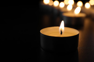 Burning candle on table in darkness, closeup with space for text. Funeral symbol