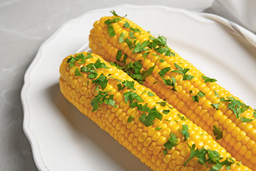 Plate with delicious boiled corn cobs and parsley on light table