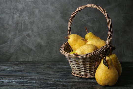 Basket of fresh ripe pears on table against gray background with space for text