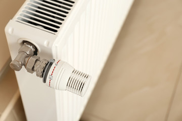 Heating radiator with thermostat near wall indoors, closeup