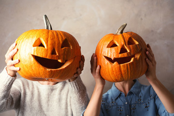 Women holding Halloween pumpkin head jack lanterns against color background