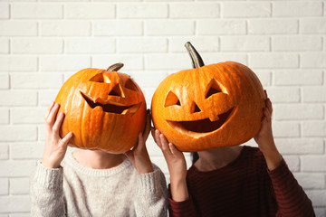 Women holding Halloween pumpkin head jack lanterns against brick wall