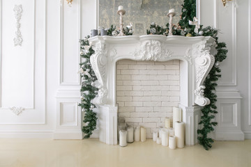 White fireplace decorated with candles and fir branches. Decorated Christmas tree. Classic apartments, morning in hotel