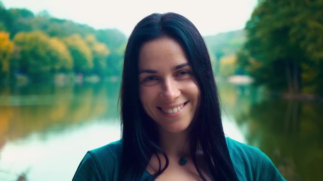 Portrait of a young smiling woman with black hair. A girl with dimples. Woman near the lake at sunset of the day.