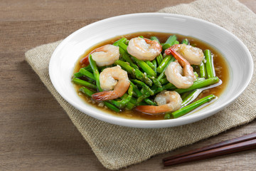 stir fried asparagus and shrimp with oyster sauce in a ceramic dish on wooden table. asian homemade style food concept.