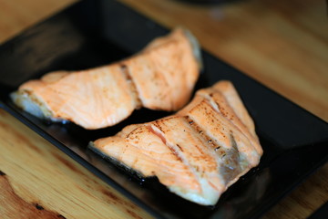 Fototapeta na wymiar Grilled salmon on black dish with dipping soy sauce and green spicy sauce on wooden table