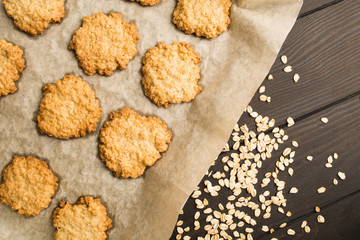 Oatmeal cookies over baking paper with oat on wooden background