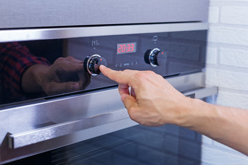 Man hand setting cooking mode on electrical oven. Male finger press button on control panel on oven, close up