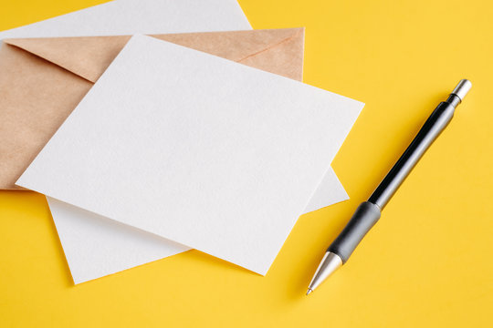 White Paper Empty Sheets Cards, Kraft Envelope And Pen On A Yellow Background. Mockup For Design