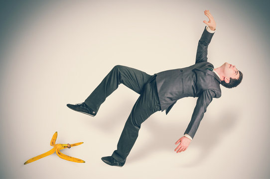 Businessman slipping and falling from a banana peel