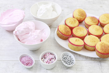 Woman prepares muffins decorated with cream and sprinkles.