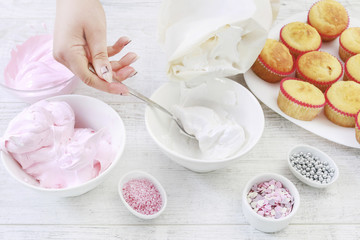 Obraz na płótnie Canvas Woman prepares muffins decorated with cream and sprinkles.