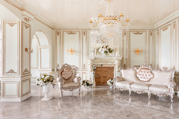 Morning in luxurious light interior in mansion . Bright and clean interior design of a luxury living room with stone floors, fireplace, sofa and chair . Stucco on walls