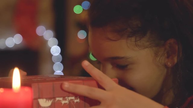 Young little girl opening Christmas gift box and looking inside with golden magic light coming from it