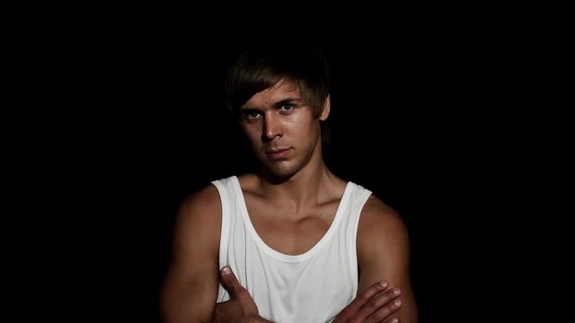 Young sporty attractive caucasian blue eyed man with nice haircut dressed in white shirt and blue tight jeans, standing, looking at camera and smiling on black matt background