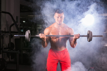 Bodybuilder doing the exercises with barbell. Strong male with naked torso on dark background. Strength and motivation.