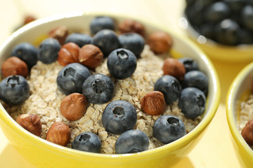 oatmeal porridge with blueberries and hazelnuts. Muesli with berries and nuts.granola and fresh blueberries in a yellow  bowl on a yellow  plank background.Useful breakfast.Healthy Eating