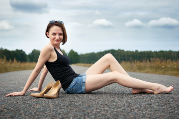 young girl sitting barefoot on the road, she left her shoes on the road and forgot them, the concept of summer and travel