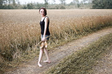 young girl walking barefoot on the ground road through field and forest, the concept of summer and travel